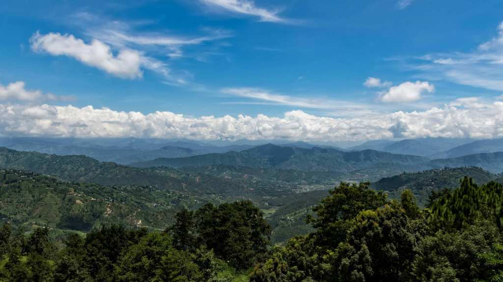 A view from Dhulikhel showcasing green rolling hills and a blue sky.
